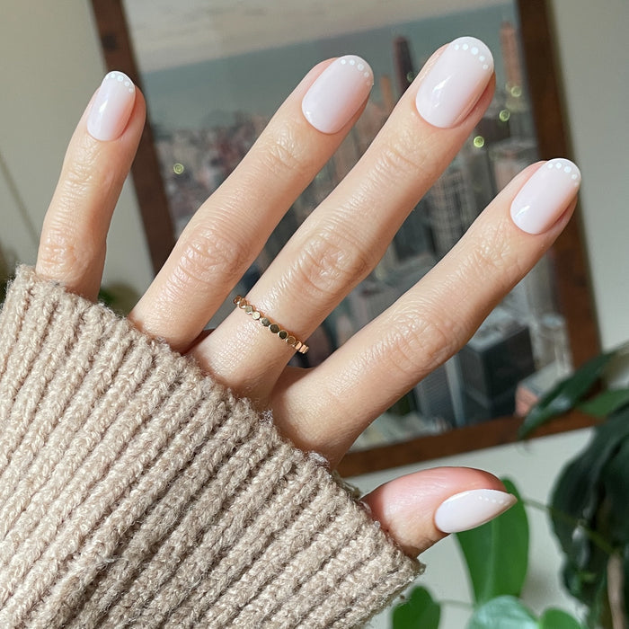 Dotted French | Short | Round - Tab Press-On nails in soft pink with white dot French tips shown on hand in cozy beige sweater