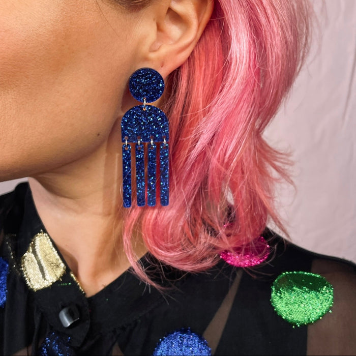Close-up of a person wearing blue tassel earrings with pink hair.
