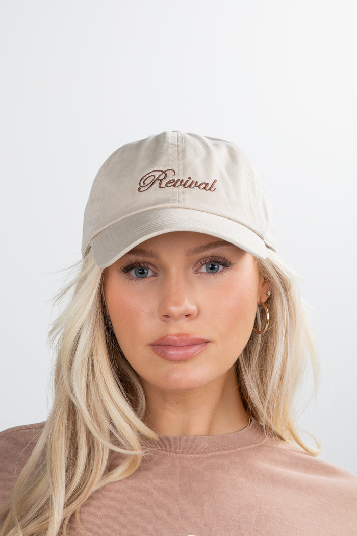 Woman wearing a beige cap with 'Revival' text on a white background