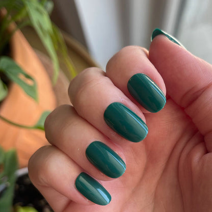 Besties - Press-On | Short | Round showing hand with glossy deep emerald green short round press-on manicure indoors near plants