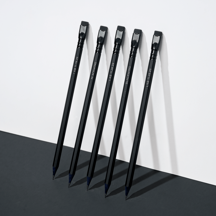 five black pencils leaning against a white wall