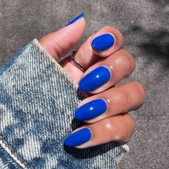 Medium-length nails painted with Blueberry Muffin cobalt blue long-lasting polish against denim sleeve background