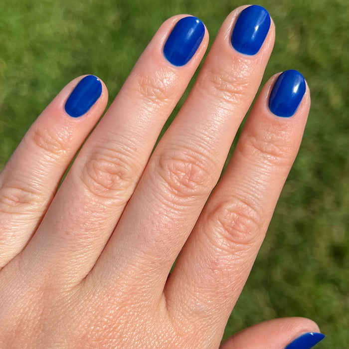 Short nails painted in vibrant Blueberry Muffin cobalt blue nail polish shown outdoors with natural light