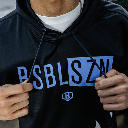 Close-up of blue BSBLSZN chest graphic and BL101 diamond logo on black short sleeve hoodie, model pulling drawstrings.