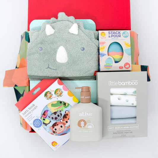A baby hamper gift set presented in a red box, including a dinosaur hooded towel, bath toys, a bath book, and a bottle of hair and body wash. Price: 135