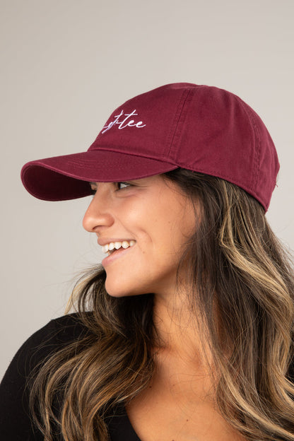 Woman wearing a maroon cap with 'coffee' embroidered on it against a neutral background