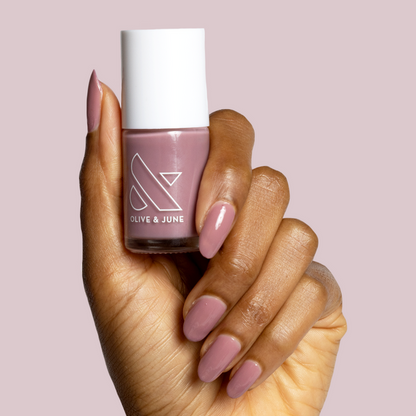 Hand with medium brown skin wearing Can I Borrow A Sweater? mauve gel polish manicure holding nail polish bottle