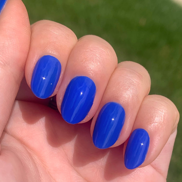 Hand with oval nails painted in vibrant Can’t Lose blue polish for a glossy, long-lasting manicure by Olive and June