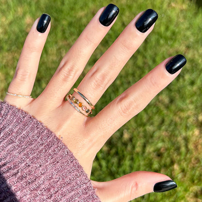 Cateye | Extra Short | Squoval - Tab Press-On nails in glossy inky black worn on hand with rings outdoors on grass background