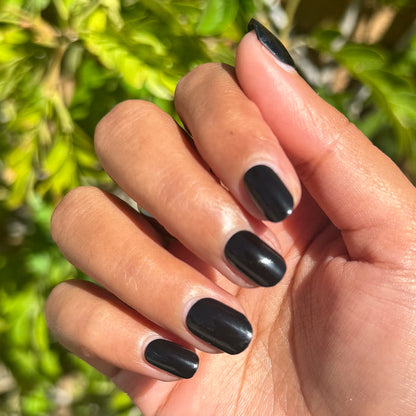 Cateye | Extra Short | Squoval - Tab Press-On nails in glossy deep black shown on hand outdoors with green foliage background