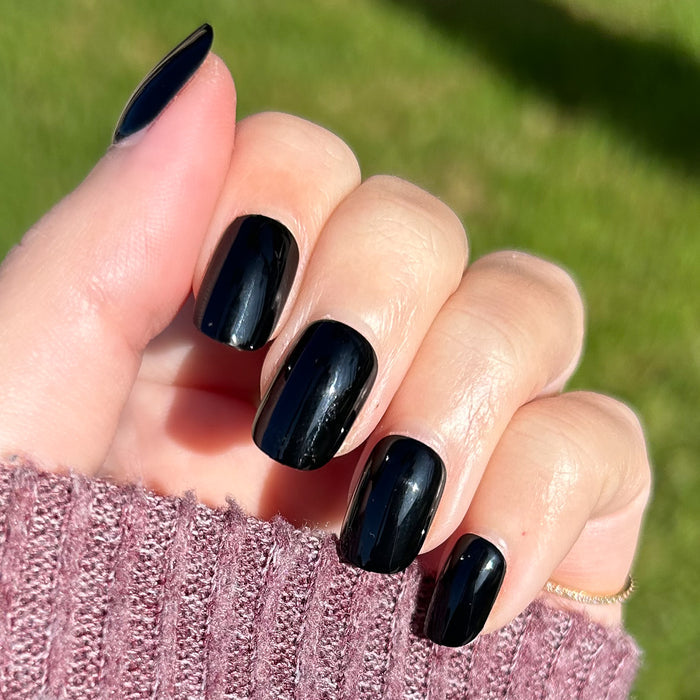 Cateye | Extra Short | Squoval - Tab Press-On nails in glossy deep black shown on hand outdoors with sunlight and sweater background