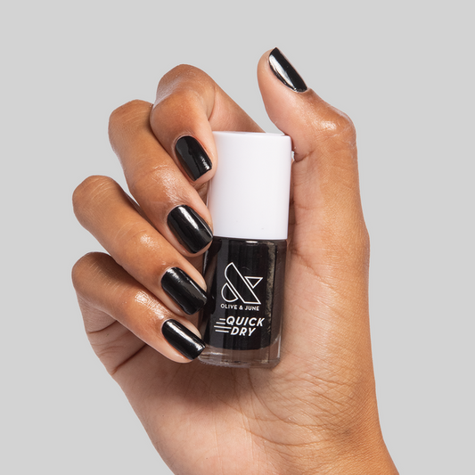 Hand with glossy black Cateye polish holding Olive and June quick dry nail polish bottle on gray background