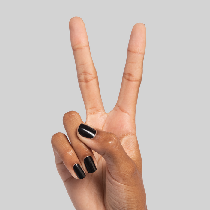 Hand displaying peace sign with nails in glossy black Cateye polish on a neutral gray background for a sleek mani