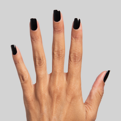 Hand with nails painted in glossy Cateye black polish showcasing a sleek mani against a light gray background