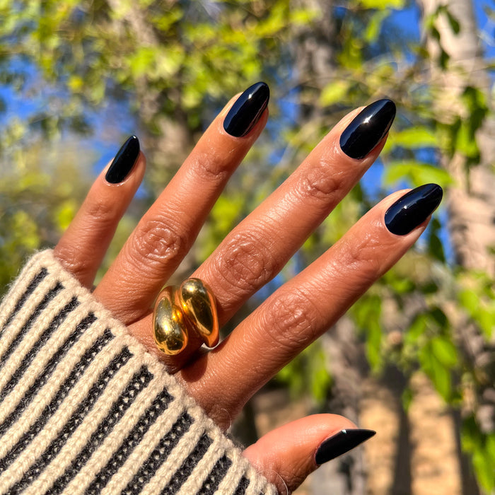 Hand with shiny black Cateye polish on almond-shaped nails outdoors with sunlight and a striped sweater sleeve