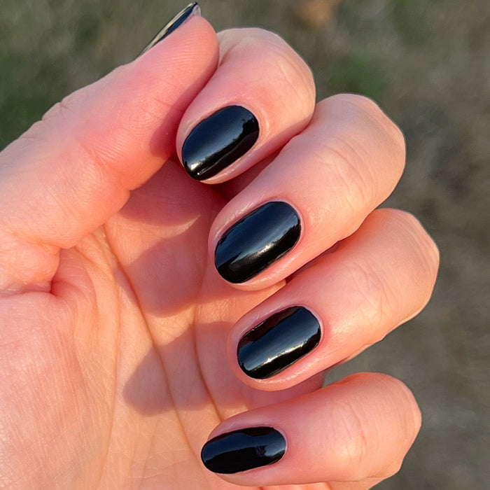 Hand with short nails painted in glossy Cateye black polish shown outdoors in natural sunlight for a shiny mani