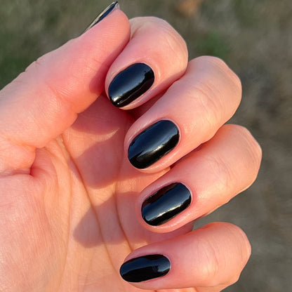 Hand with short nails painted in glossy Cateye black polish shown outdoors in natural sunlight for a shiny mani