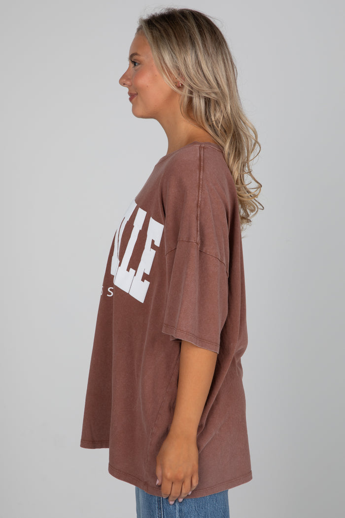 Woman wearing a brown oversized t-shirt with 'VILLE' printed on it against a plain background