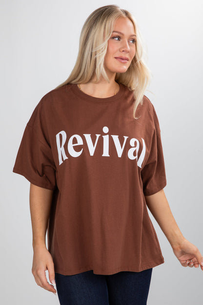 Woman wearing a brown oversized t-shirt with 'Revival' printed on it against a plain background
