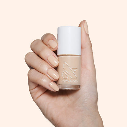 Hand holding Olive and June Coffee Milk polish bottle with nails painted in creamy neutral tan shade