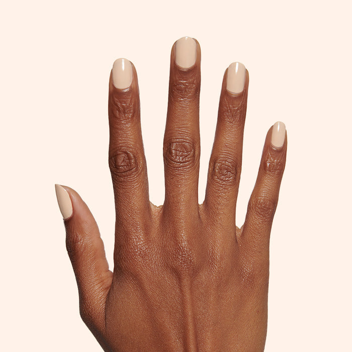 Hand with medium-length nails painted in creamy neutral tan Coffee Milk nail polish against pale background