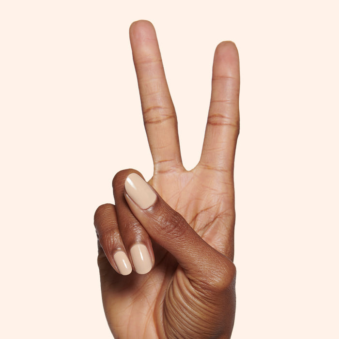 Hand with medium-length nails painted in creamy neutral tan Coffee Milk polish on light beige background