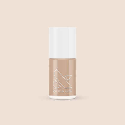 Bottle of Coffee Milk nail polish in creamy neutral tan shade by Olive and June on beige background