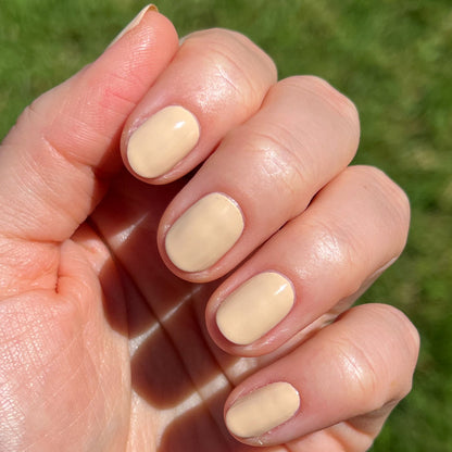 Short rounded nails painted with creamy neutral tan Coffee Milk nail polish in natural sunlight outdoors