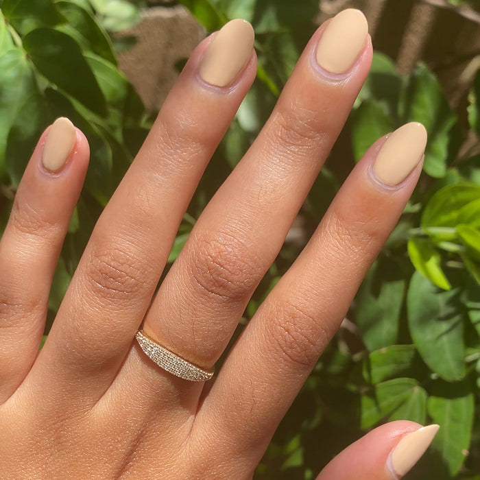 Hand with almond-shaped nails painted in matte Coffee Milk polish wearing gold band ring outdoors in sunlight