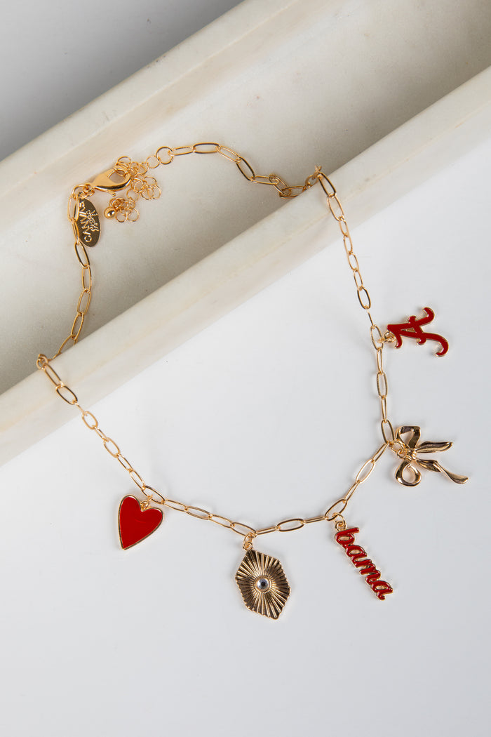 Gold bracelet with various charms including a heart, shell, and 'home' tag on a white surface.