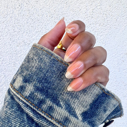 Hand with natural nails polished in Crystal clear coat holding a denim jacket sleeve showing a glossy manicure