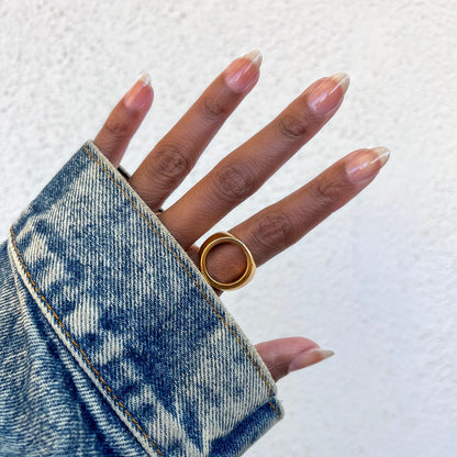 Hand with nails coated in Crystal glossy polish wearing a gold ring and denim jacket sleeve against a white wall background