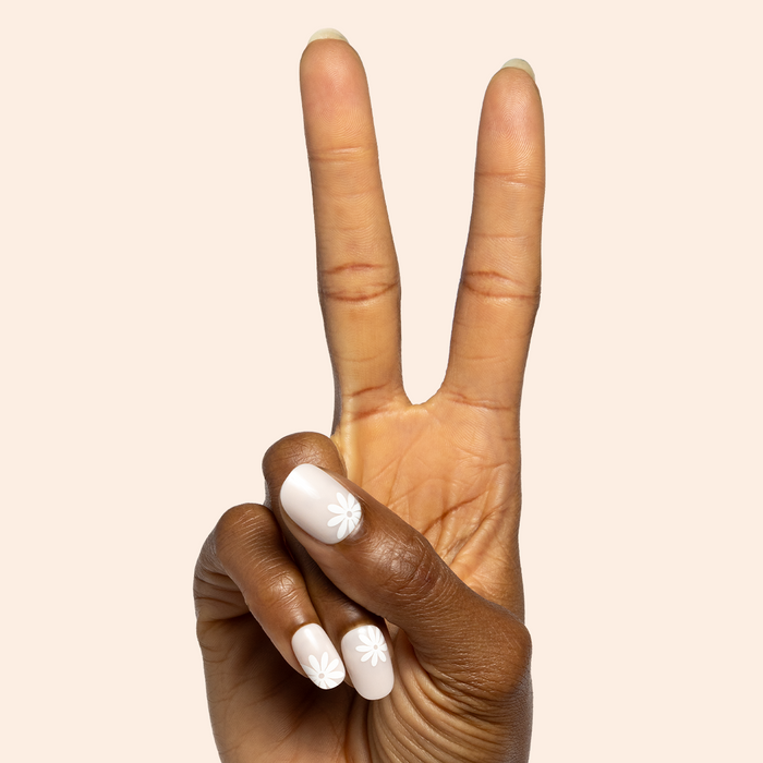 Daisy Pop | Short | Round - Tab Press-On featuring short round neutral nails with white daisy floral design on hand showing peace sign