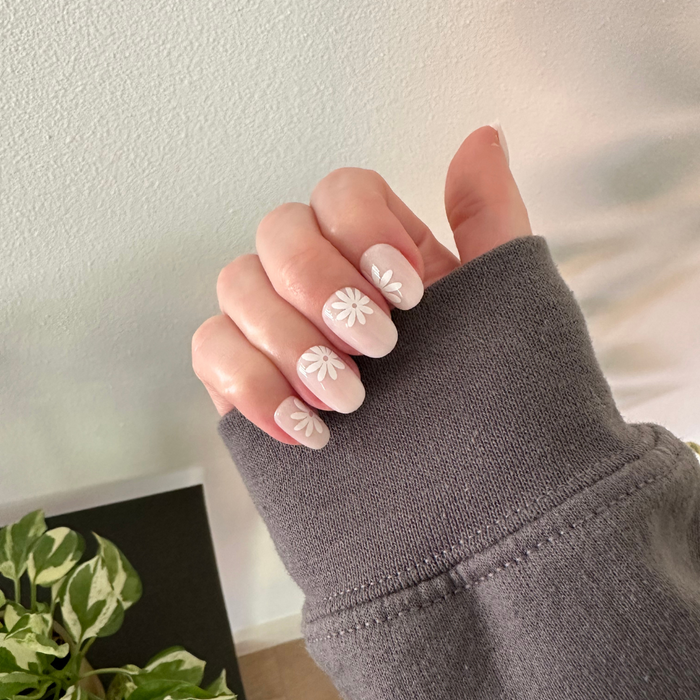 Daisy Pop | Short | Round - Tab Press-On nails with large white daisies on a soft neutral base shown on hand in cozy grey sweater