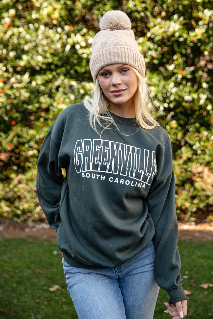 Woman wearing a dark green sweatshirt with 'Greenville, South Carolina' text, standing outdoors.