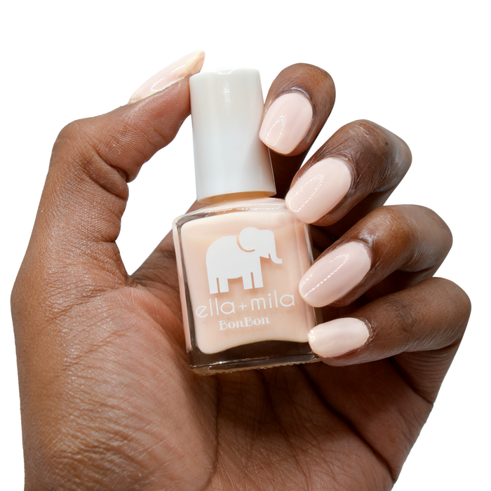 Dessert Island nude shimmer nail polish on a deep skin tone, hand holding the bottle