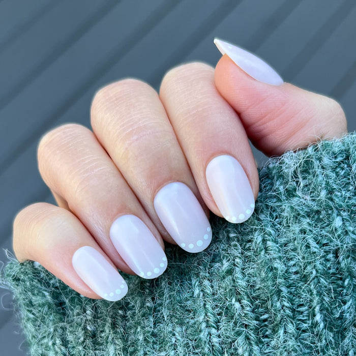Dotted French | Short | Round - Tab Press-On nails with subtle white dot tips on short round nails held in green knit sweater