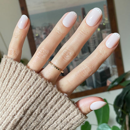 Dotted French | Short | Round - Tab Press-On nails in soft pink with white dot French tips shown on hand in cozy beige sweater