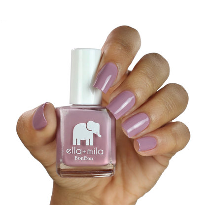 Dulce Amor dusty lavender rose nail polish on a medium skin tone, hand holding the bottle