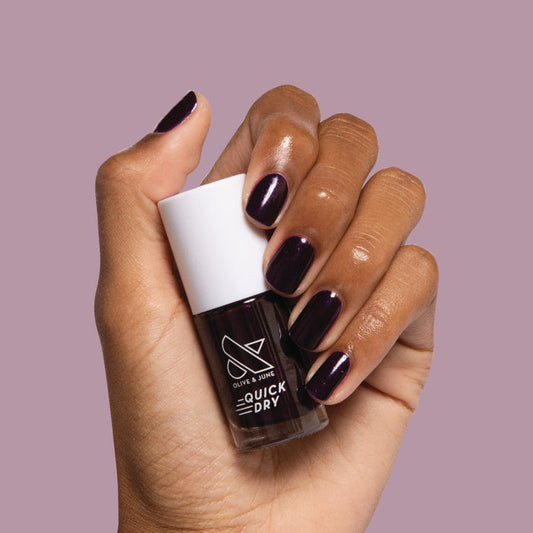 Hand holding bottle of Enchanted nail polish with nails painted in dark shimmery violet for a manicure