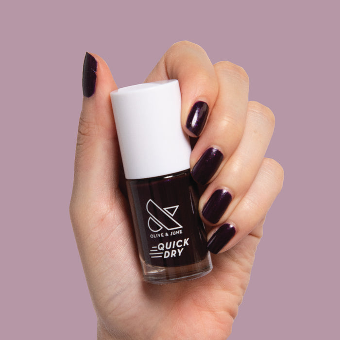 Hand holding Enchanted nail polish with nails painted in dark shimmering violet for a quick dry mani by Olive and June
