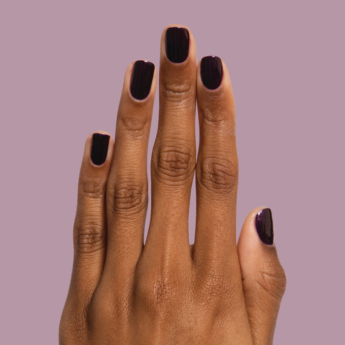 Hand with nails painted in dark shimmery violet Enchanted polish for a striking at-home manicure by Olive and June