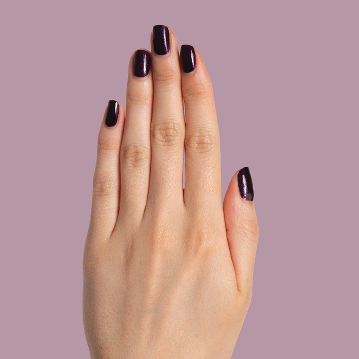 Hand with nails painted in dark shimmery violet Enchanted polish for a polished at-home manicure by Olive and June