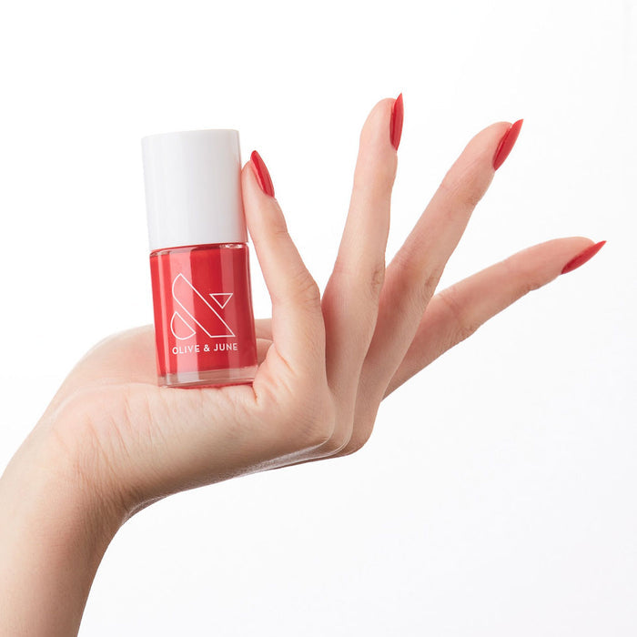 Hand holding bottle of ES nail polish showing bright crimson red long-lasting manicure on natural skin tone