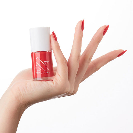 Hand holding bottle of ES nail polish showing bright crimson red long-lasting manicure on natural skin tone