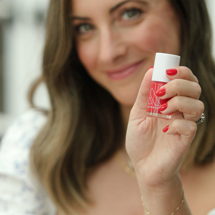 Woman holding a bottle of ES nail polish showing bright crimson red long-lasting manicure on natural skin tone