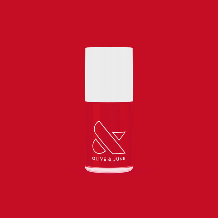 Bottle of ES nail polish in bright classic crimson red by Olive and June on a matching red background