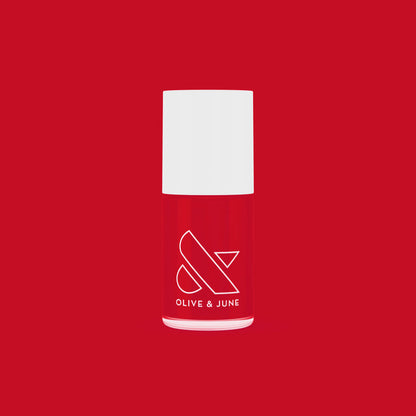 Bottle of ES nail polish in bright classic crimson red by Olive and June on a matching red background