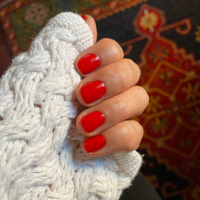 Hand with nails painted in ES polish showing smooth, vibrant crimson red manicure against knitted white fabric background