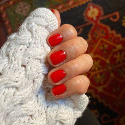 Hand with nails painted in ES polish showing smooth, vibrant crimson red manicure against knitted white fabric background